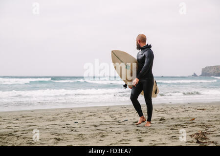 Un surfista passeggiate in dall'acqua dopo un giorno di onde in Big Sur, California.