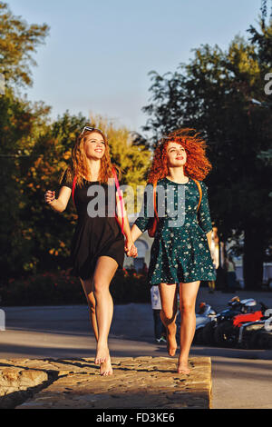 Migliori amici studenti di sesso femminile in un parco della città. Ragazza camminare a piedi nudi nel parco. Le ragazze vanno mano nella mano. Foto Stock