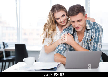 Felice bella giovane utilizzando laptop insieme seduti a tavola a casa Foto Stock