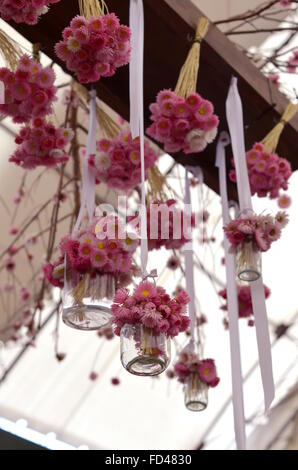 Decorazione fatta di mazzetti di margherite rosa, vasetti di vetro e nastri bianchi Foto Stock