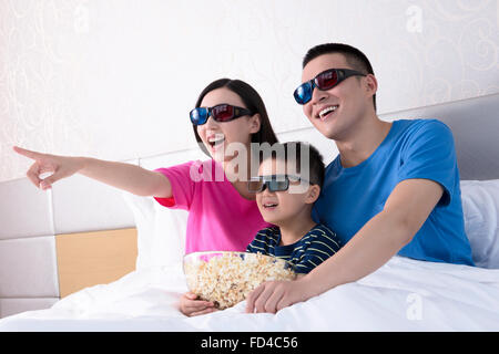 Famiglia a guardare la TV in 3D nel letto con popcorn Foto Stock