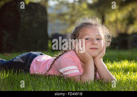 Felice giovane ragazza che stabilisce in erba al parco Foto Stock