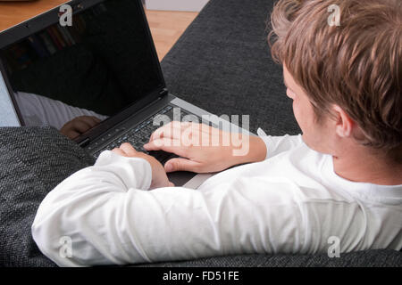 Giovane uomo disteso sul lettino e di lavoro sul computer portatile- concentrarsi sulle mani e il computer Foto Stock