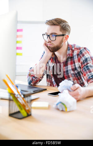 Considerato giovane uomo con la barba in plaid shirt lavorando e la deformazione della carta in ufficio Foto Stock