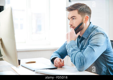 Malinconici attraente maschio barbuto designer in jeans shirt pensare e rendere blueprint utilizzando una penna di Tablet Foto Stock