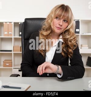 Imprenditrice guardando lei guarda come si siede alla sua scrivania, in attesa di un incontro che indica che qualcuno è in ritardo Foto Stock