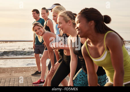 Un gruppo di giovani atleti in posizione di avviamento, si concentrano sulla donna. Montare i giovani preparazione gara lungo il mare. Foto Stock