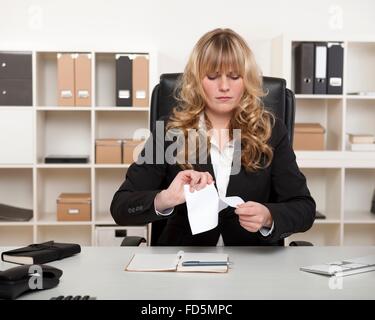 Giovane imprenditrice seduto alla sua scrivania con un look di concentrazione di poppa la lacerazione di un documento che mostra il suo dispiacere Foto Stock