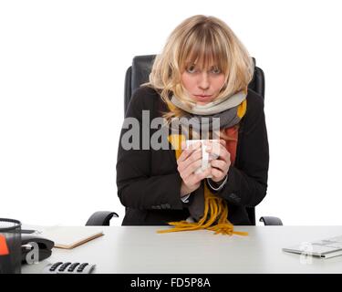 Freddo imprenditrice indossare una maglia Sciarpa invernale seduta curvò fino alla sua scrivania in fase di riscaldamento con una tazza di caffè caldo Foto Stock