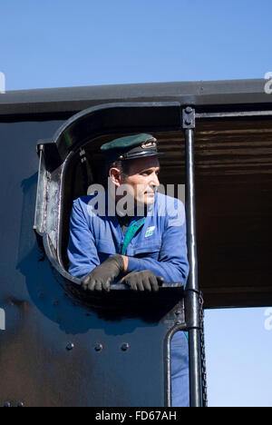 Treno a vapore conducente guardando fuori della sua cabina in corrispondenza di una stazione di fermata Foto Stock