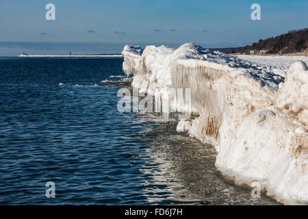 Ghiaccioli formata da spruzzare del lago Michigan onde si infrangono contro una cresta di ghiaccio, con Grand Haven faro a distanza Foto Stock