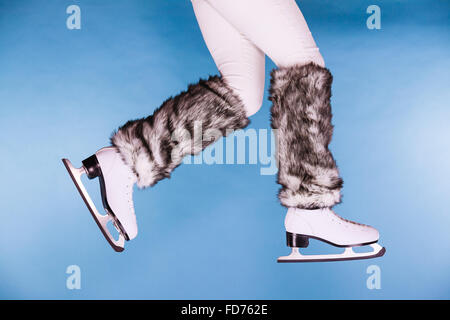Donna gambe indossando pattini pelliccia calze calde. Ragazza ottenere pronto per il pattinaggio su ghiaccio. Sport invernali attività. Studio shot su blu Foto Stock