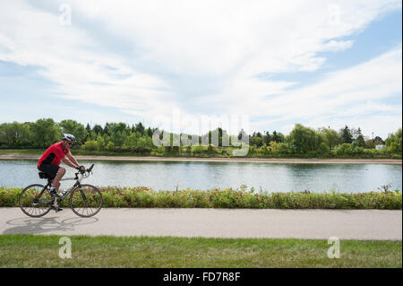 Ciclista in sella insieme a waterfront bike trail su un giorno d'estate. Foto Stock