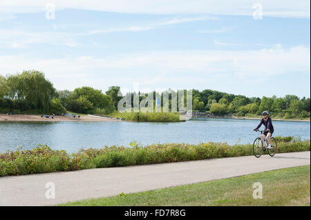 Ciclista in sella insieme a waterfront bike trail su un giorno d'estate. Foto Stock