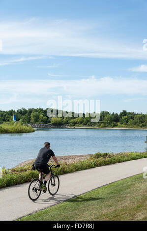 Ciclista in sella insieme a waterfront bike trail su un giorno d'estate. Foto Stock