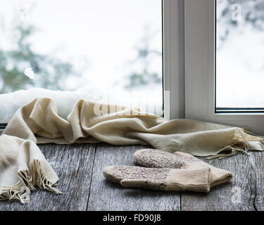 Beige sciarpa di lana e muffole situato sul legno stilizzata davanzale. Inverno concetto di comfort e relax. Foto Stock