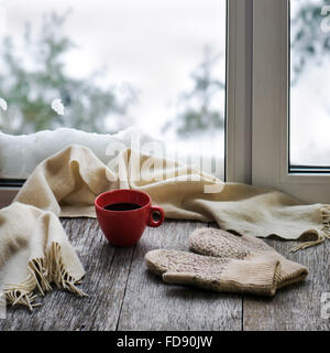 Red tazza di caffè o di tè, beige sciarpa e womans guanti sono situati sul legno stilizzata davanzale. Inverno concetto di comfort di un Foto Stock