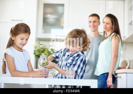 Due bambini di acqua potabile con lime fresco in cucina mentre i genitori stanno a guardare Foto Stock