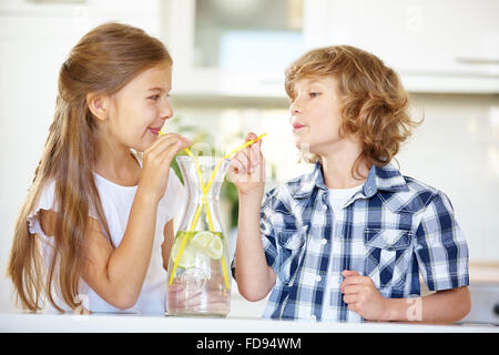 Due bambini di bere acqua fresca con paglia in cucina Foto Stock