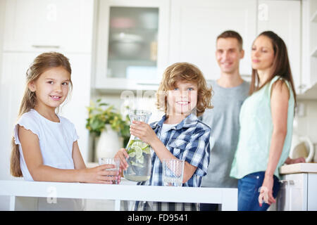 Due bambini con caraffa di bere acqua fresca con calce in cucina Foto Stock