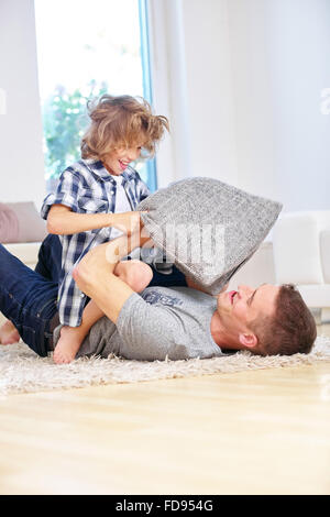 Felice padre e figlio facendo cuscino lotta in casa nel salotto Foto Stock