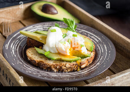 Uovo affogato e avocado su tutta tostati pane di frumento con semi su una piastra in legno vintage vassoio. Guarnito con lo scalogno Foto Stock