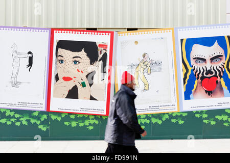 Un uomo che indossa un rosso brillante beanie hat passeggiate da un Mac poster Conner al King's Cross riconvertire a Londra, Inghilterra. Foto Stock