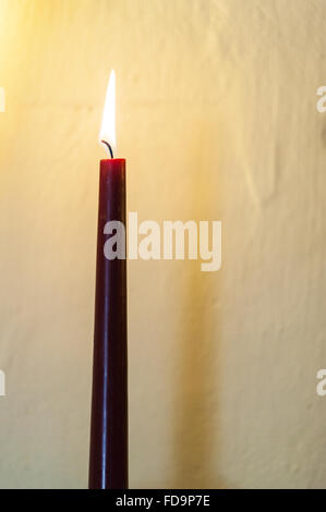 Una candela accesa accanto a una parete Foto Stock