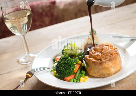 Torta e purè di patate e verdure su un piatto con il sugo di carne che viene colato e con un bicchiere di vino. Un pasto da pub. Foto Stock