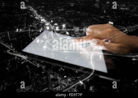 La doppia esposizione mano utilizzando tablet e città su sfondo di notte Foto Stock