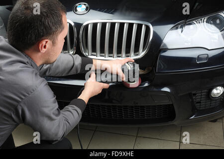 Il lavoratore lucidi un bumper car cruscotto con l'attrezzo elettrico. Servizio auto. Foto Stock