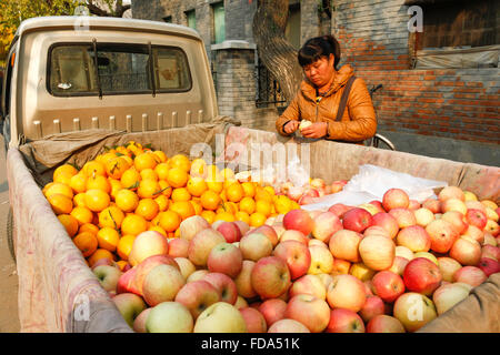 Donna cinese per la vendita di frutta da carrello; la spesa per produrre in un mercato all'aperto nel centro di Pechino, Cina. Foto Stock