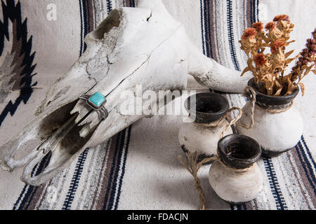Cranio di mucca intemperie, bracciale con polsino turchese e argento, ceramica messicana dipinta in bianco e nero con fiori secchi su una coperta a strisce messicane. Foto Stock