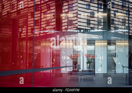 Un vaso di fiori di colore rosso che riflette in un vetro frontale in ufficio edificio reception, Southwark London REGNO UNITO Foto Stock