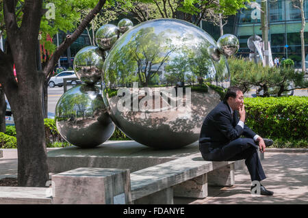 Uomo seduto e il fumo da arte moderna, relection sfere, al di fuori del COEX Mall, Samseong-dong, Gangnam-gu, Seoul, Corea del Sud Foto Stock