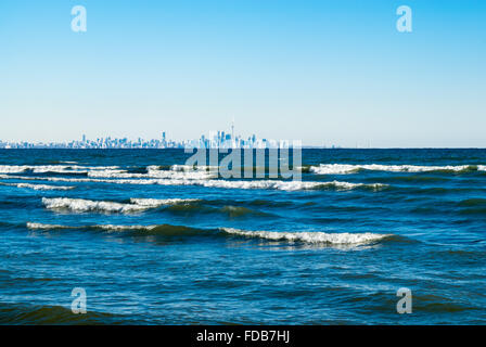 Onde che si infrangono sulle acque azzurre del lago Ontario, contro il cielo blu chiaro con toronto skyline della città lontano in distanza. Foto Stock