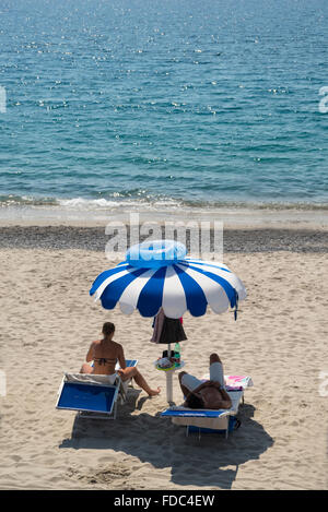 Coppia giovane sulla sdraio con blu e bianco ombrellone e nuotare anello sulla parte superiore del Mingardo spiaggia,Cilento,Campania,Italia Foto Stock