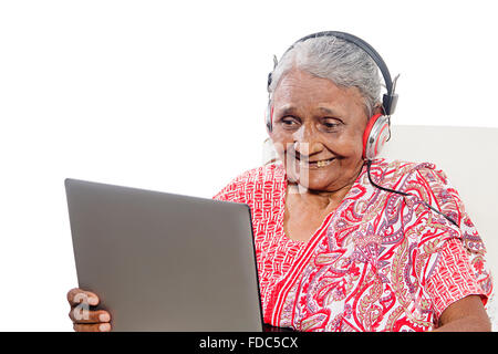 1 adulti senior donna seduta divano di lavoro portatile e le cuffie Ascolto della musica Foto Stock