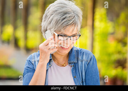 Bella donna matura il giardinaggio e parlando al telefono Foto Stock