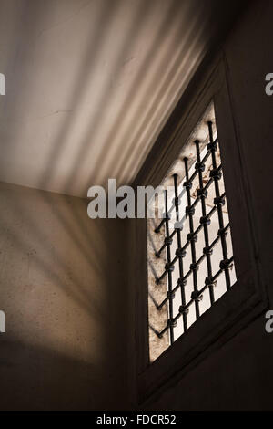Cella di prigione con la luce che brilla attraverso una finestra sbarrata in camera Foto Stock