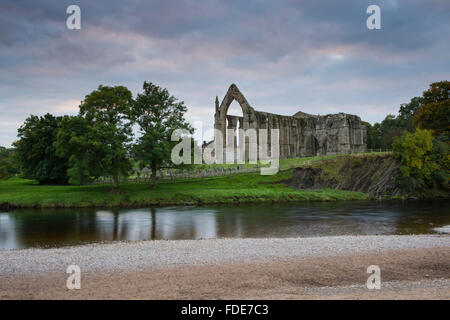 Convento agostiniano rovine a Bolton Abbey su una sera d'autunno, attraverso l'acqua del fiume Wharfe e la sua spiaggia di ciottoli - North Yorkshire, Inghilterra, Regno Unito Foto Stock