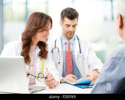 Il team medico di discutere il trattamento con senior paziente di sesso maschile mentre è seduto alla sala di consultazione. Foto Stock