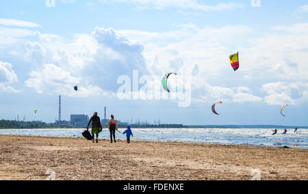 Sosnovy Bor, Russia - Luglio 19, 2015: Famiglia di camminare sulla spiaggia. Kitesurfisti cavalcare le onde del golfo di Finlandia Foto Stock