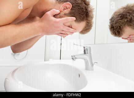Lavaggio uomo il suo volto nel lavandino del bagno Foto Stock
