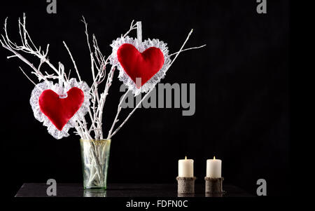 Coppia di cuori rossi su un ramo con due candele Foto Stock
