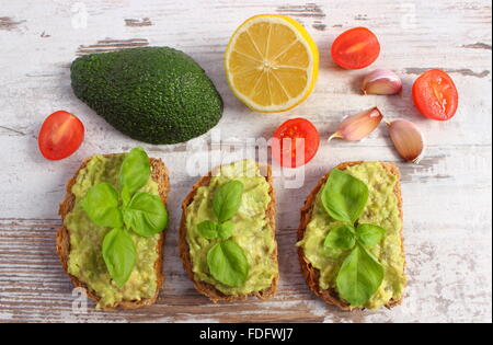 Ingredienti e panini freschi con pasta di avocado, pane di segale, pomodori ciliegini, limone, aglio, basilico, Foto Stock