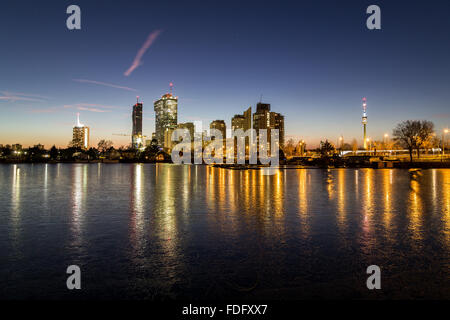 Una vista di edifici nei pressi di Alte Donau a Vienna. Presi in inverno al tramonto. Ghiaccio congelato può essere visto sul lago. Foto Stock