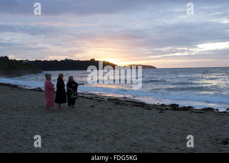 Tre donne preparano per andare il nuoto in acque libere a Gyllyngvase Beach, Falmouth di sunrise Foto Stock