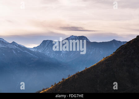 Ultima luce solare che colpisce una ripida cresta in primo piano con scenic cloudscape e moody sky sulla maestosa montagna snocapped rang Foto Stock
