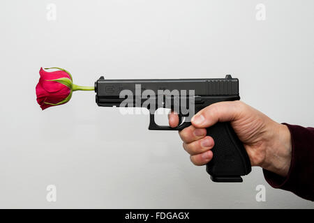 Man mano con pistola e rosa rossa nella canna della pistola come un simbolo di pace e di amicizia Foto Stock